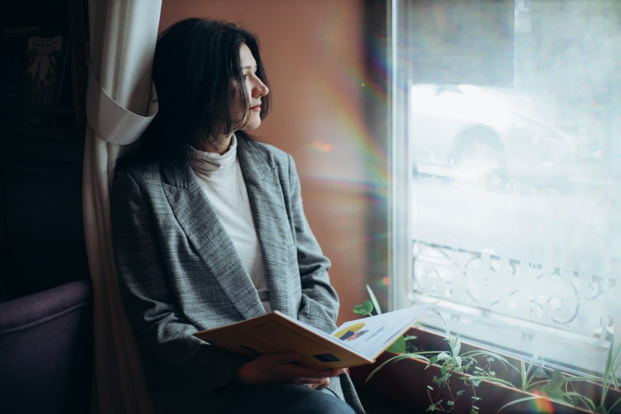 Психотерапевт Тетяна Колосова сидить на підвіконні із книгою.
