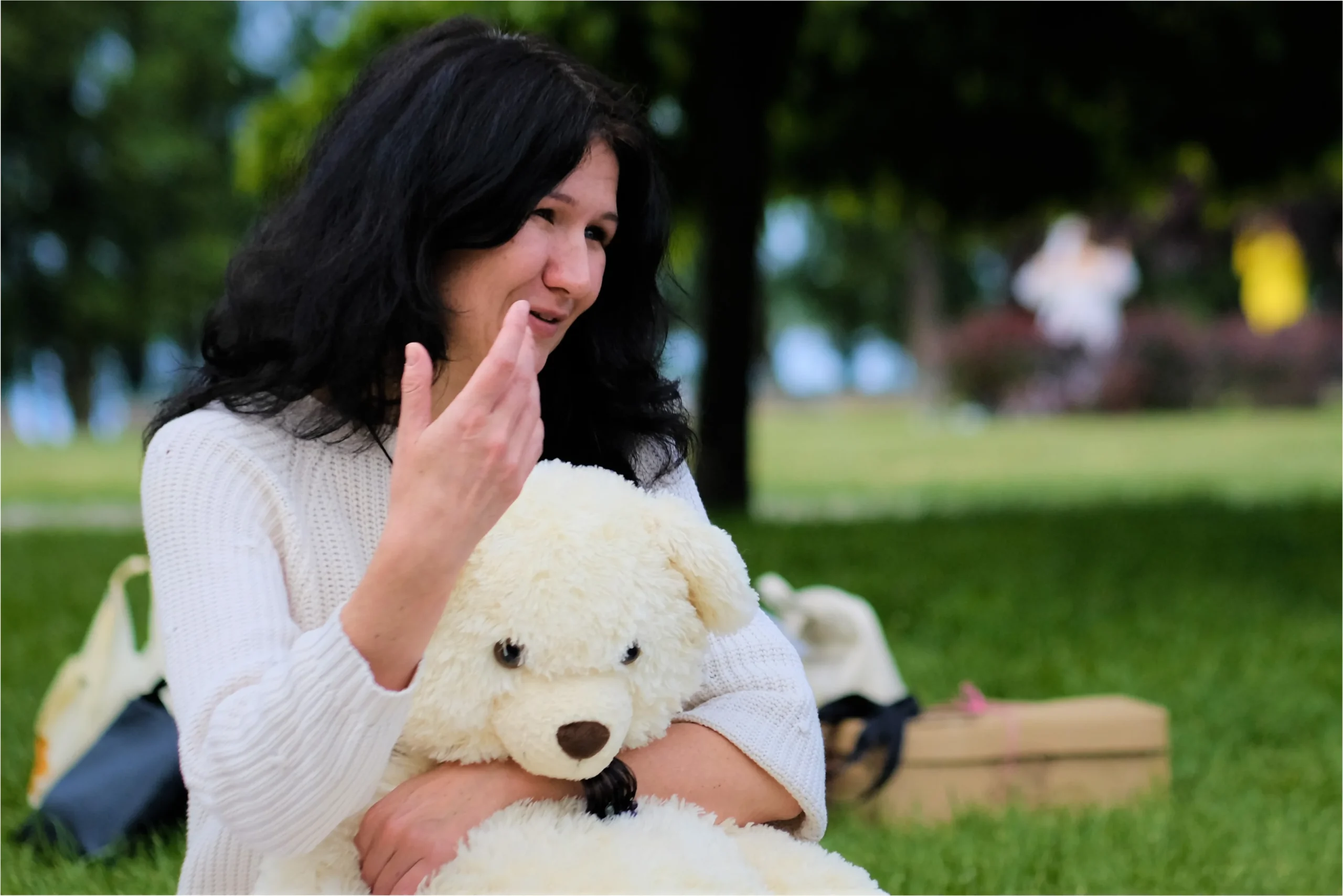 Психотерапевт Тетяна Колосова сидить на природі з великим іграшковим ведмедем в руках.